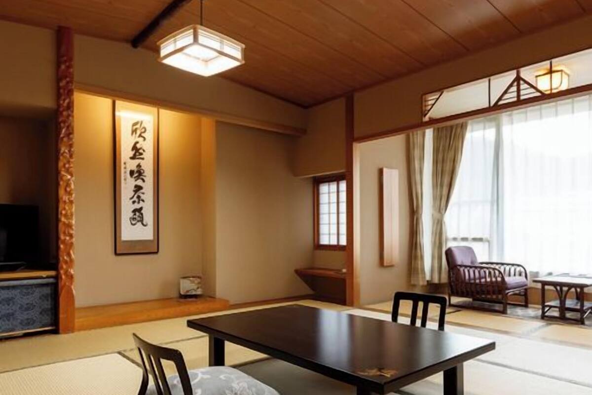 A traditional Japanese room with tatami flooring, a low table, chairs, a television, and a sliding door.
