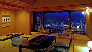 A traditional Japanese room with tatami flooring, low tables, and chairs, featuring a cityscape view through large windows. - Shogetsu (Gero)