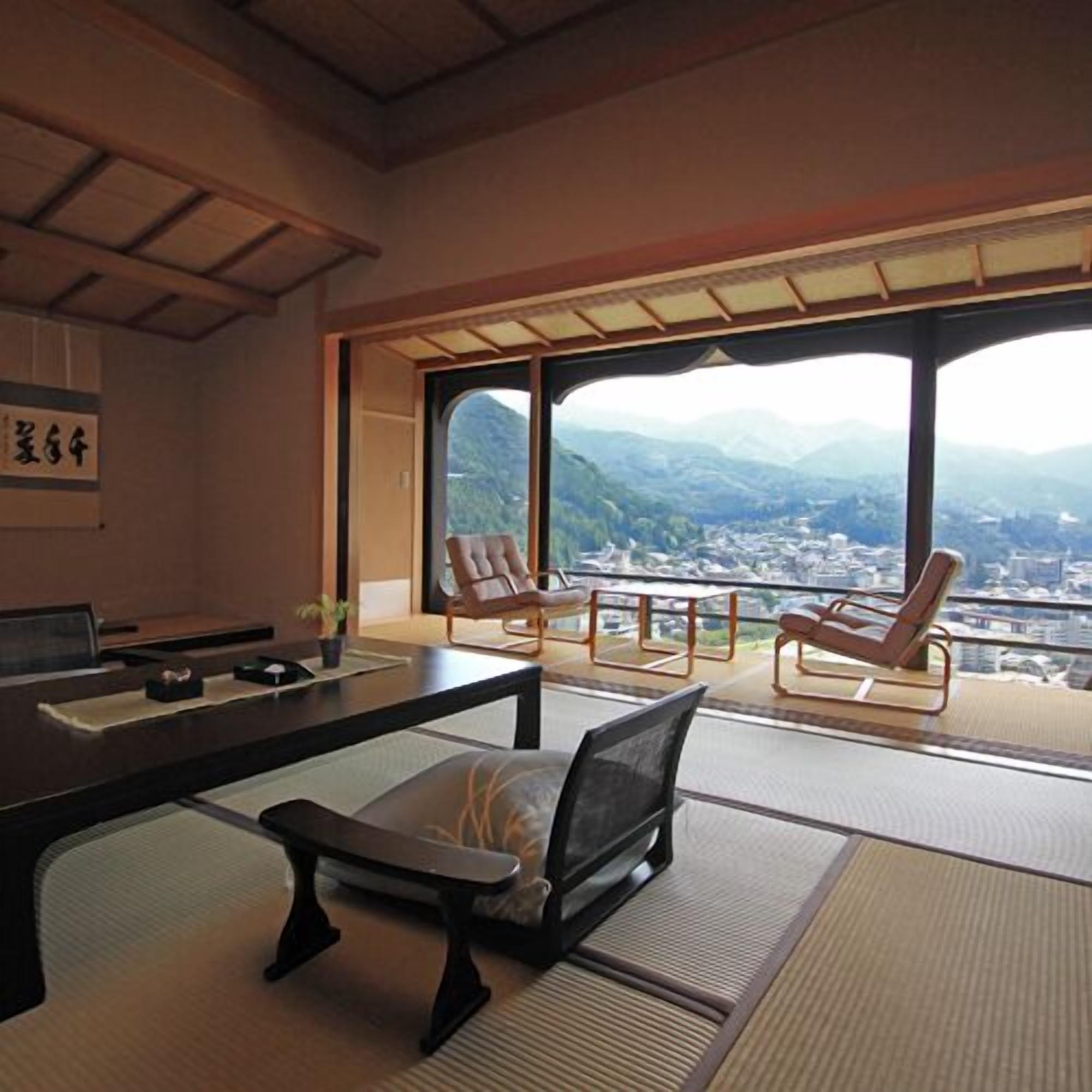 Ein traditioneller japanischer Raum mit Tatami-Bodenbelag, einem niedrigen Tisch und Blick auf eine Bergstadt.