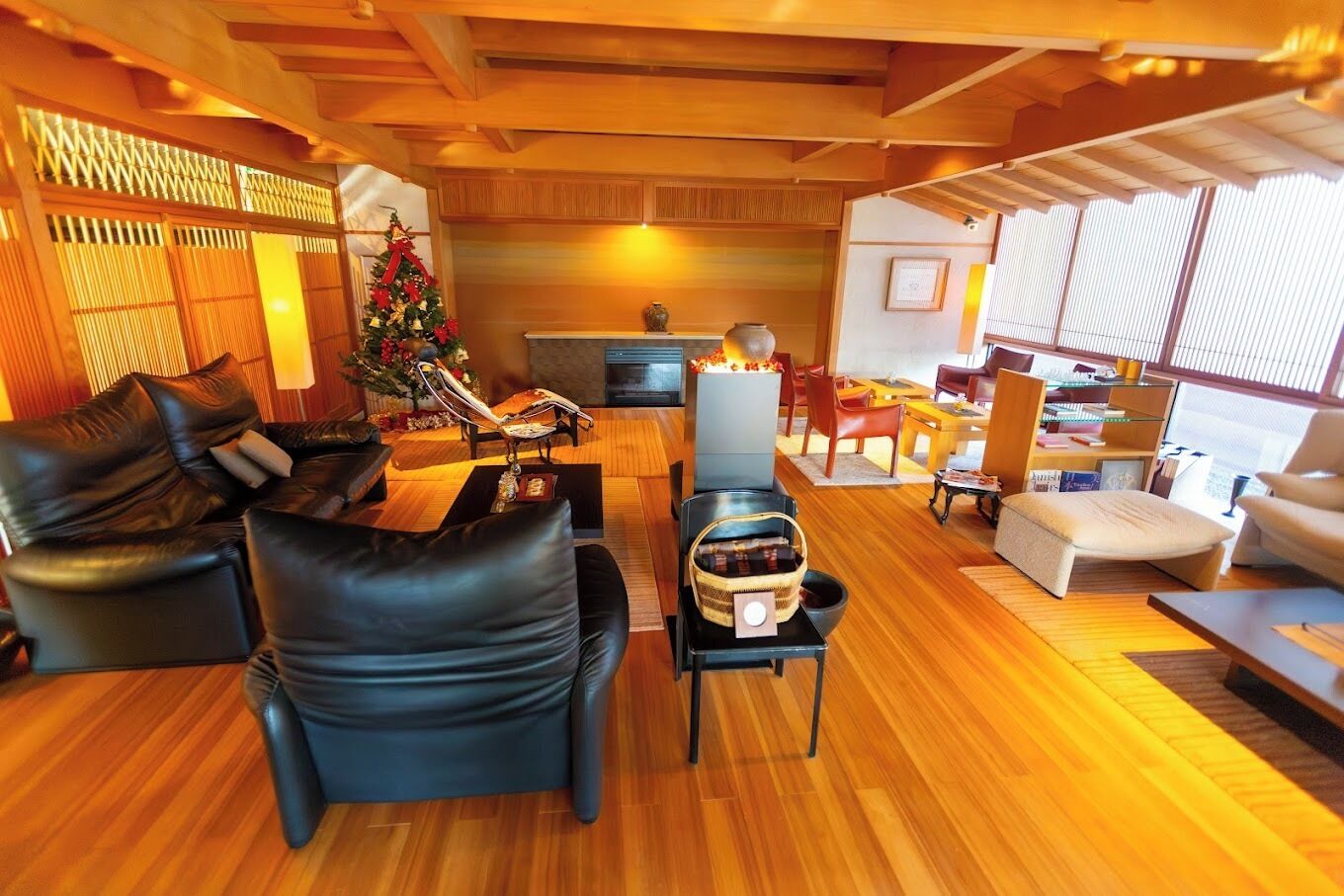 A modern living room with a wooden floor, leather sofas, a Christmas tree, and a dining area with wooden furniture.