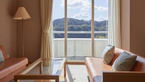 Hotellihuone, jossa on sohva, pieni pöytä ja suuret ikkunat, joista avautuu näkymä vuoristomaisemaan.