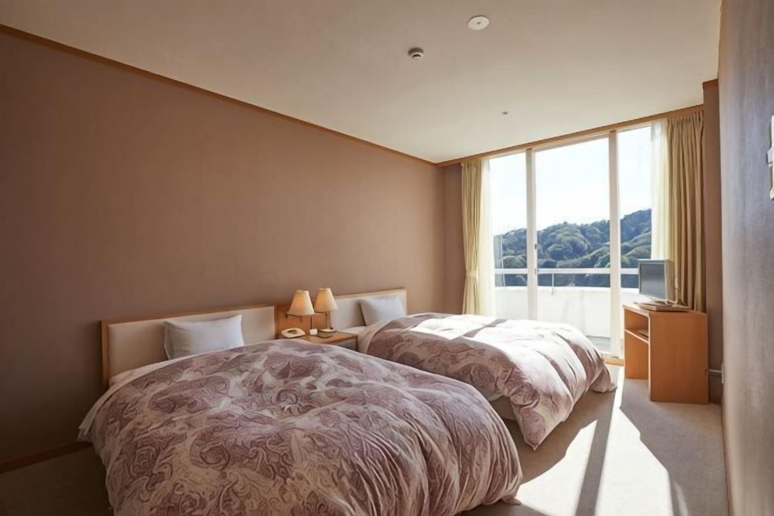 A hotel room with two beds, a large window, and a view of the outdoors.