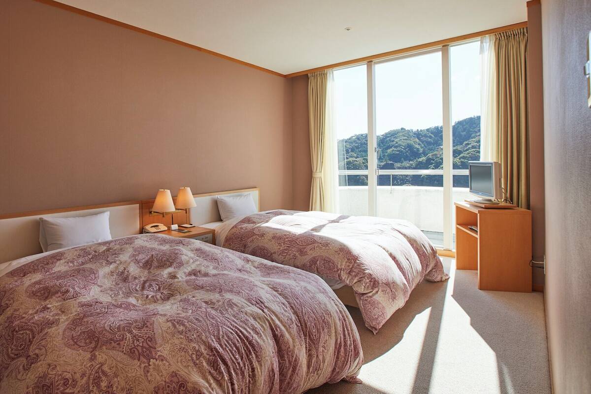 A hotel room with two beds, a TV, and a view of a mountainous landscape.