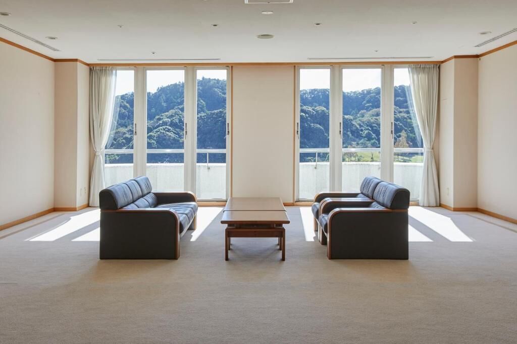 A room with two sofas facing a large window, a small table in the center, and a view of a mountainous landscape.