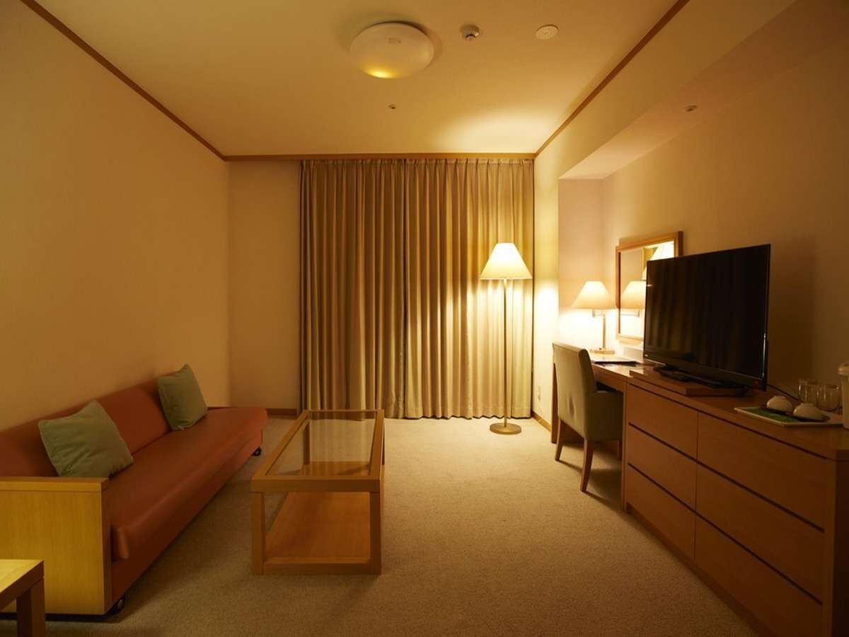 Ein Hotelzimmer mit Sofa, Glastisch, Fernseher, Schreibtisch und Lampe.