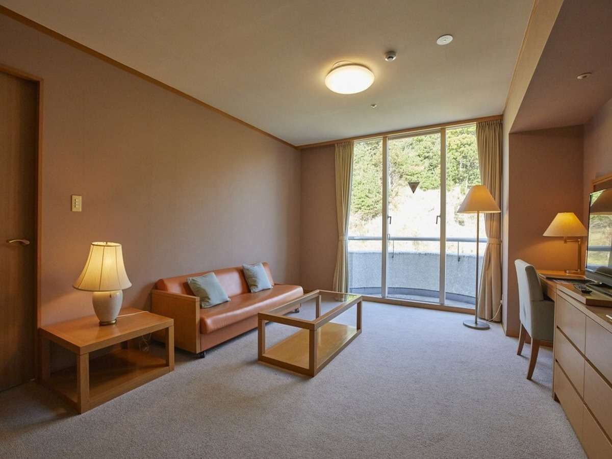 A modern hotel room with a sofa, coffee table, desk, and lamps.
