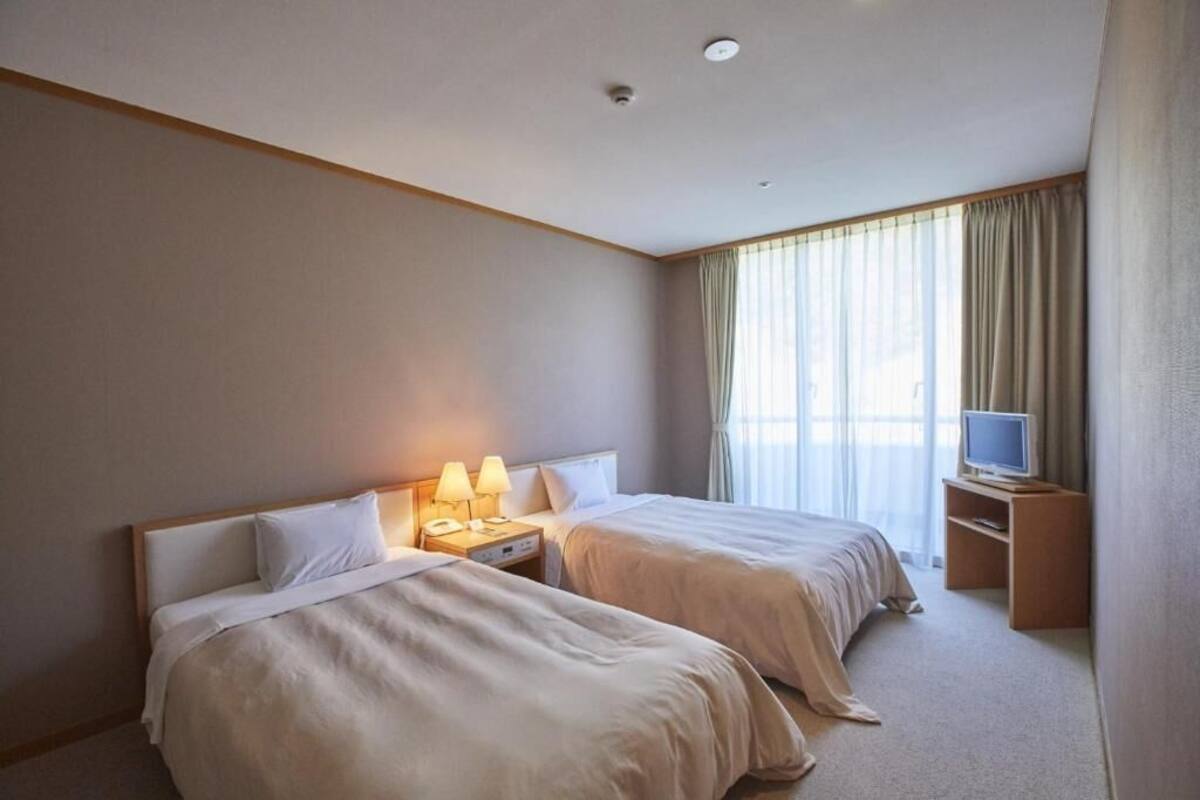 A hotel room with two beds, a television on a stand, and a window with curtains.