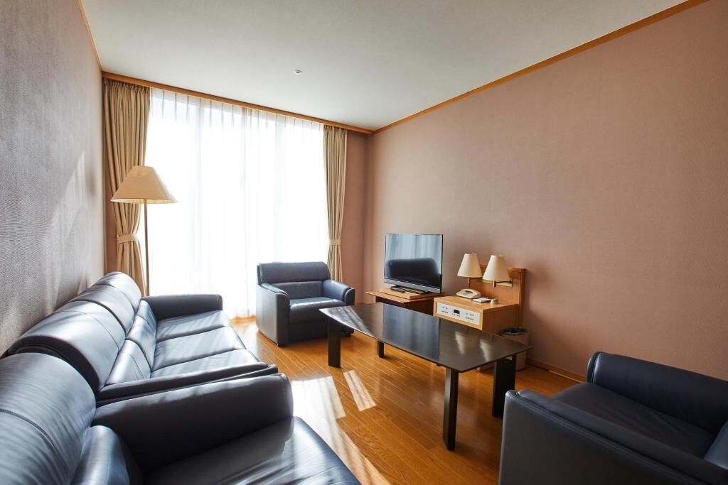 A modern hotel room with a leather sofa set, a flat-screen TV, a small table, and a lamp.