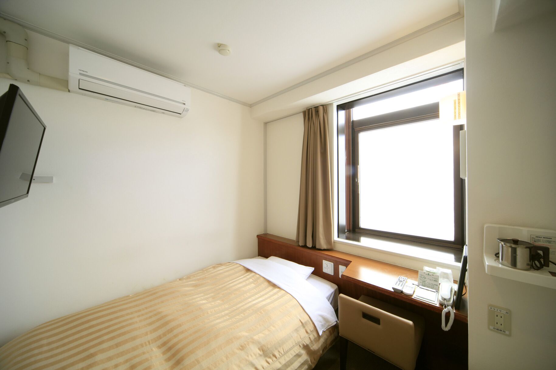 Hotelkamer met een bed, een bureau met telefoon, een raam met gordijnen en een airconditioner.