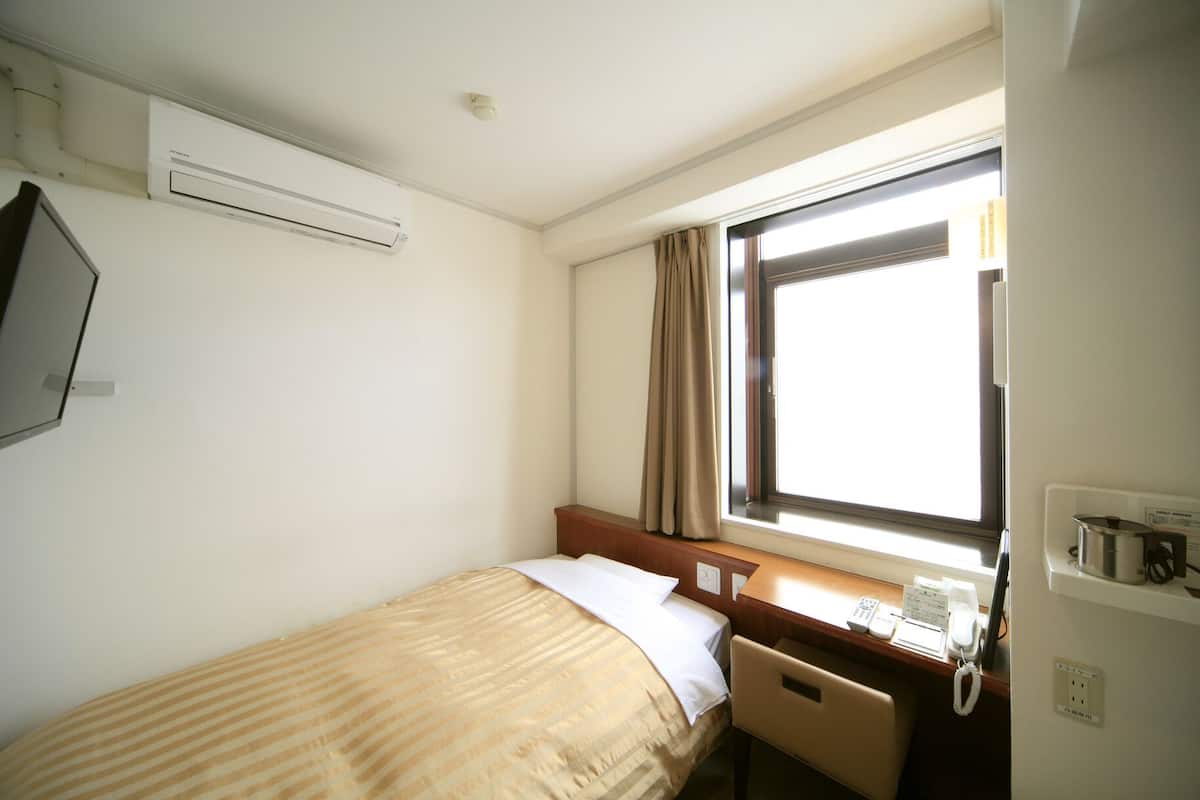 Une chambre d’hôtel équipée d’un lit, d’un bureau avec un téléphone, d’une fenêtre avec des rideaux et d’un appareil de climatisation.