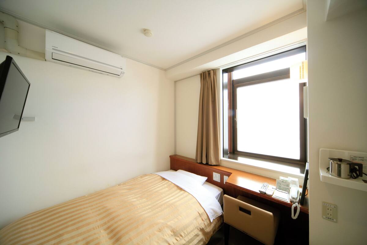 Habitació d'hotel amb llit, escriptori, telèfon i finestra amb cortines.