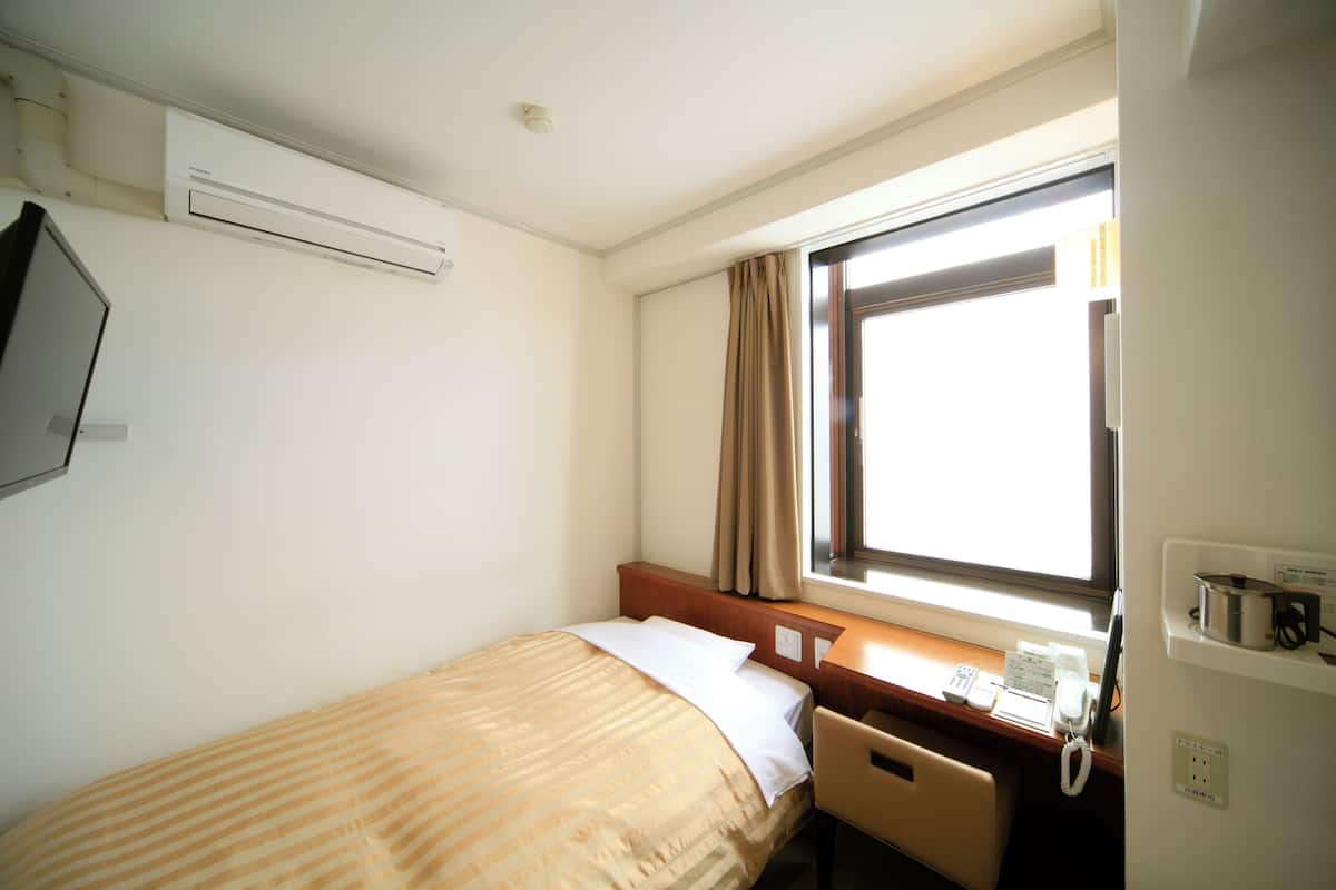 Habitación de hotel con cama, escritorio, teléfono y ventana con cortinas.