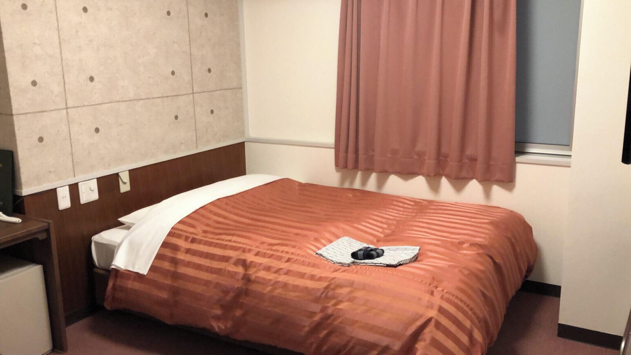 Une chambre d’hôtel avec un lit, une table de chevet, une fenêtre avec des rideaux et un mur orné d’un motif décoratif.