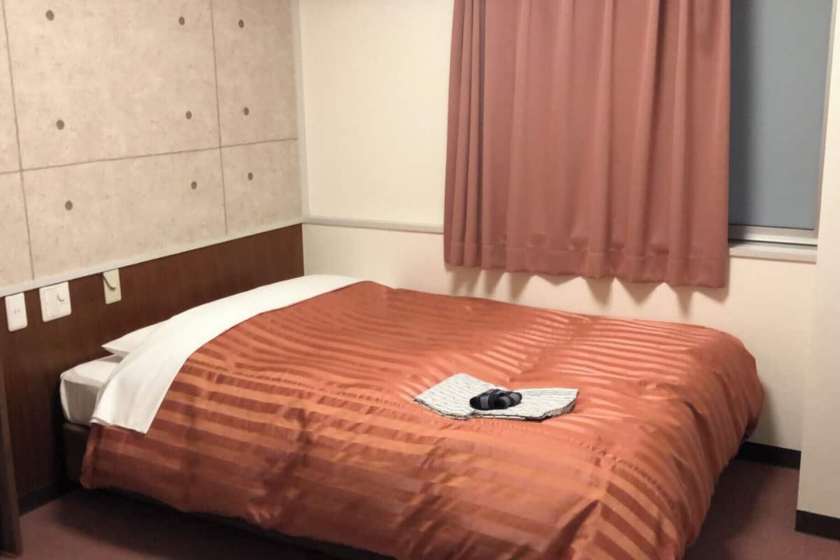 Una habitación de hotel con una cama, una mesita de noche, una ventana con cortinas y un diseño decorativo en la pared.