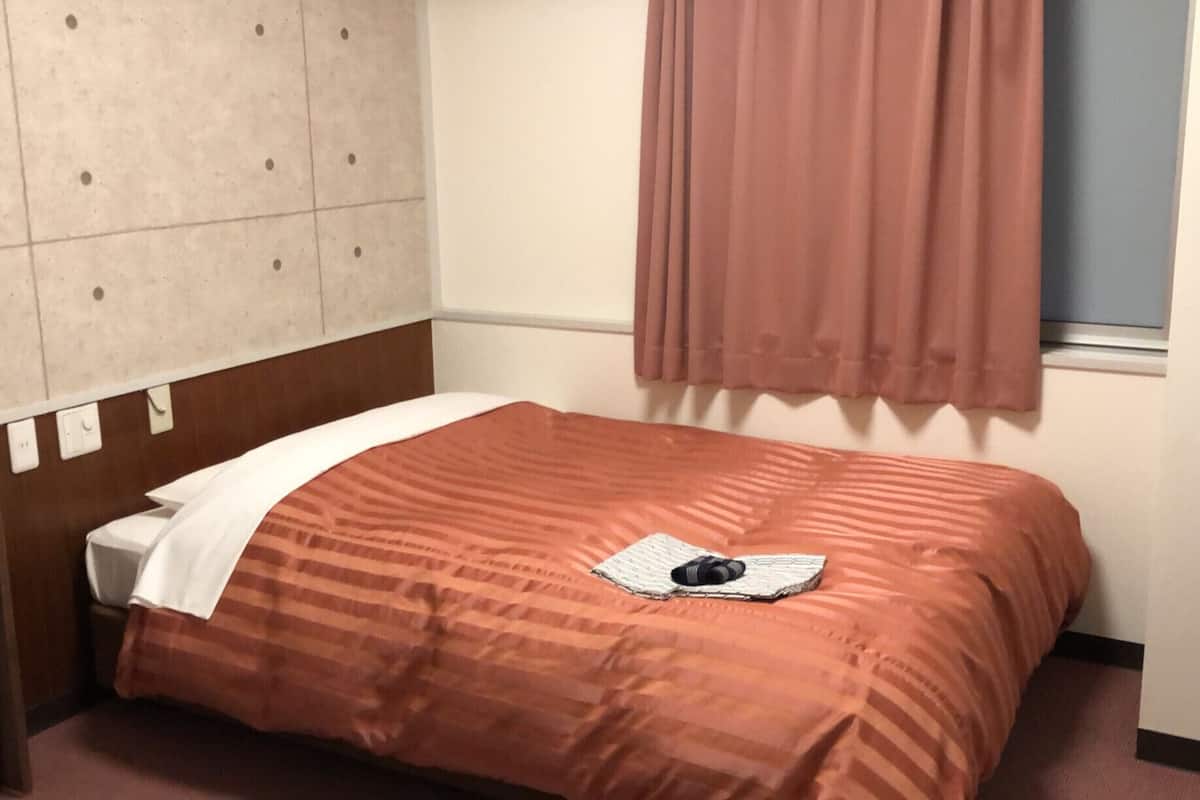 Une chambre d’hôtel avec un lit, une table de chevet, une fenêtre avec des rideaux et un mur orné d’un motif décoratif.
