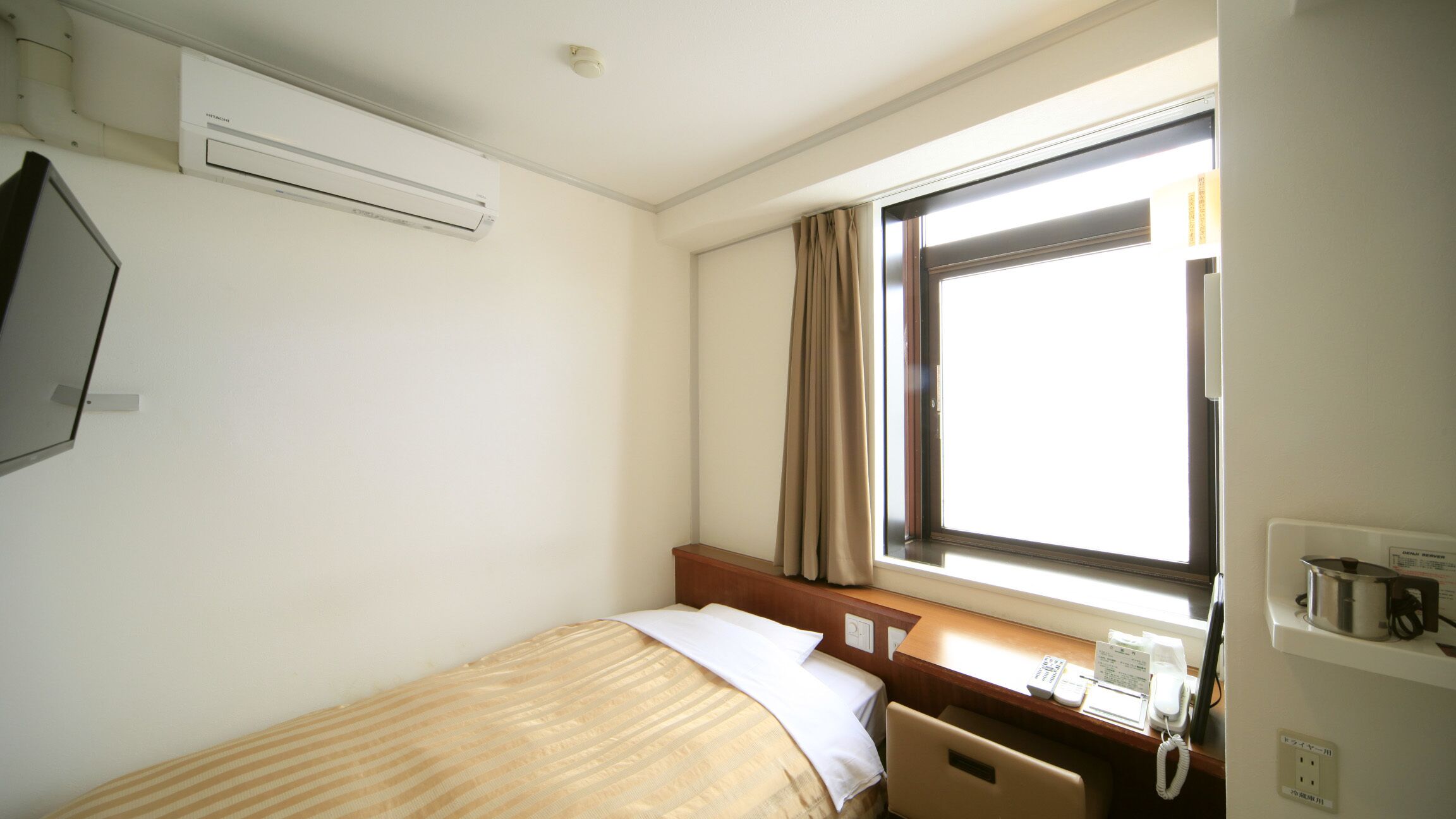 Een hotelkamer met een bed, een raam met gordijnen, een bureau met telefoon en een airconditioner aan de muur.