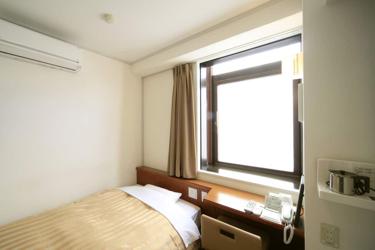 Une chambre d’hôtel avec un lit, une fenêtre avec des rideaux, un bureau avec un téléphone et un appareil de climatisation fixé au mur.