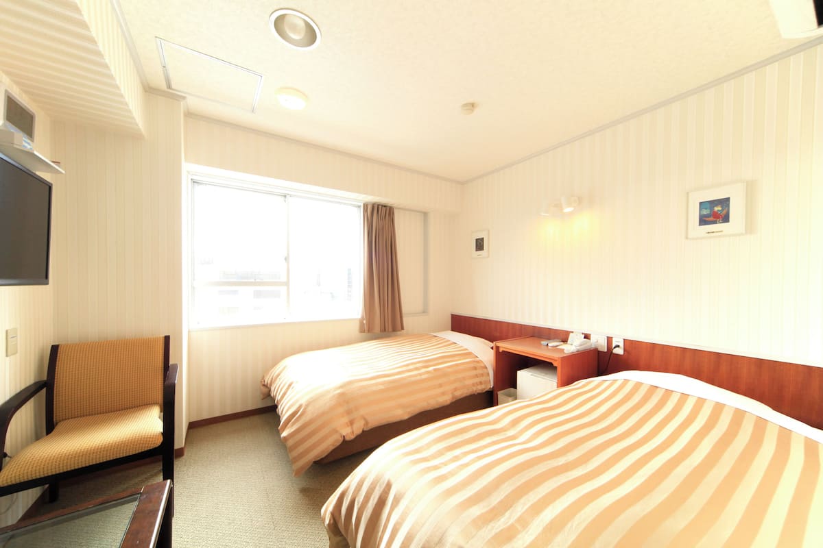 Habitación de hotel con dos camas, un escritorio, una silla, un televisor y una ventana con cortinas.