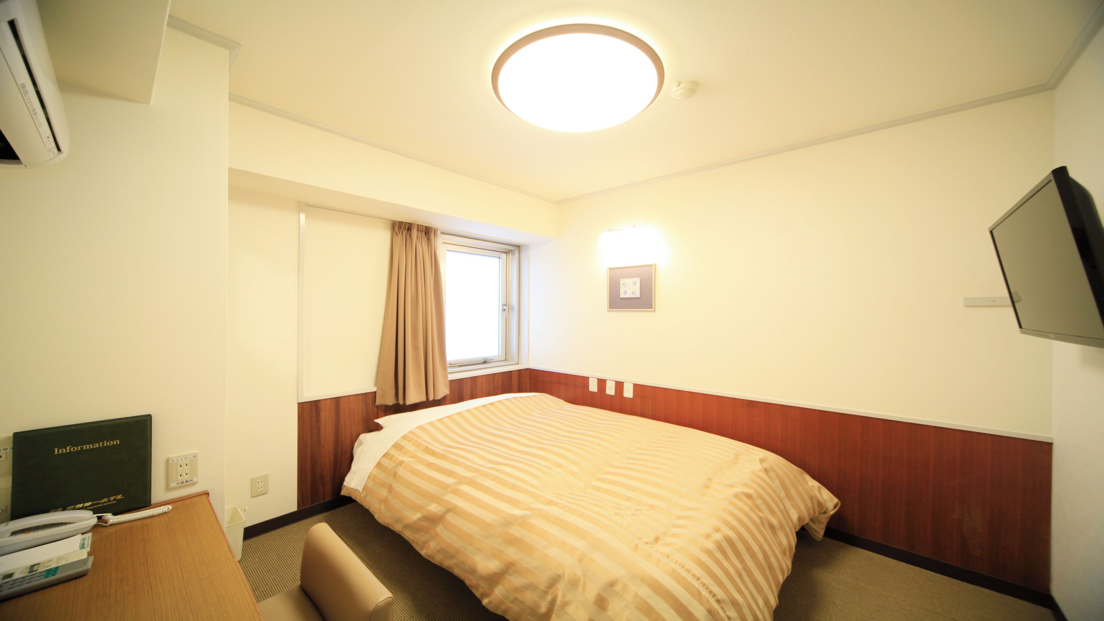 Une chambre d’hôtel comprenant un lit, un bureau avec un téléphone, un téléviseur à écran plat, une fenêtre avec des rideaux et un luminaire au plafond.