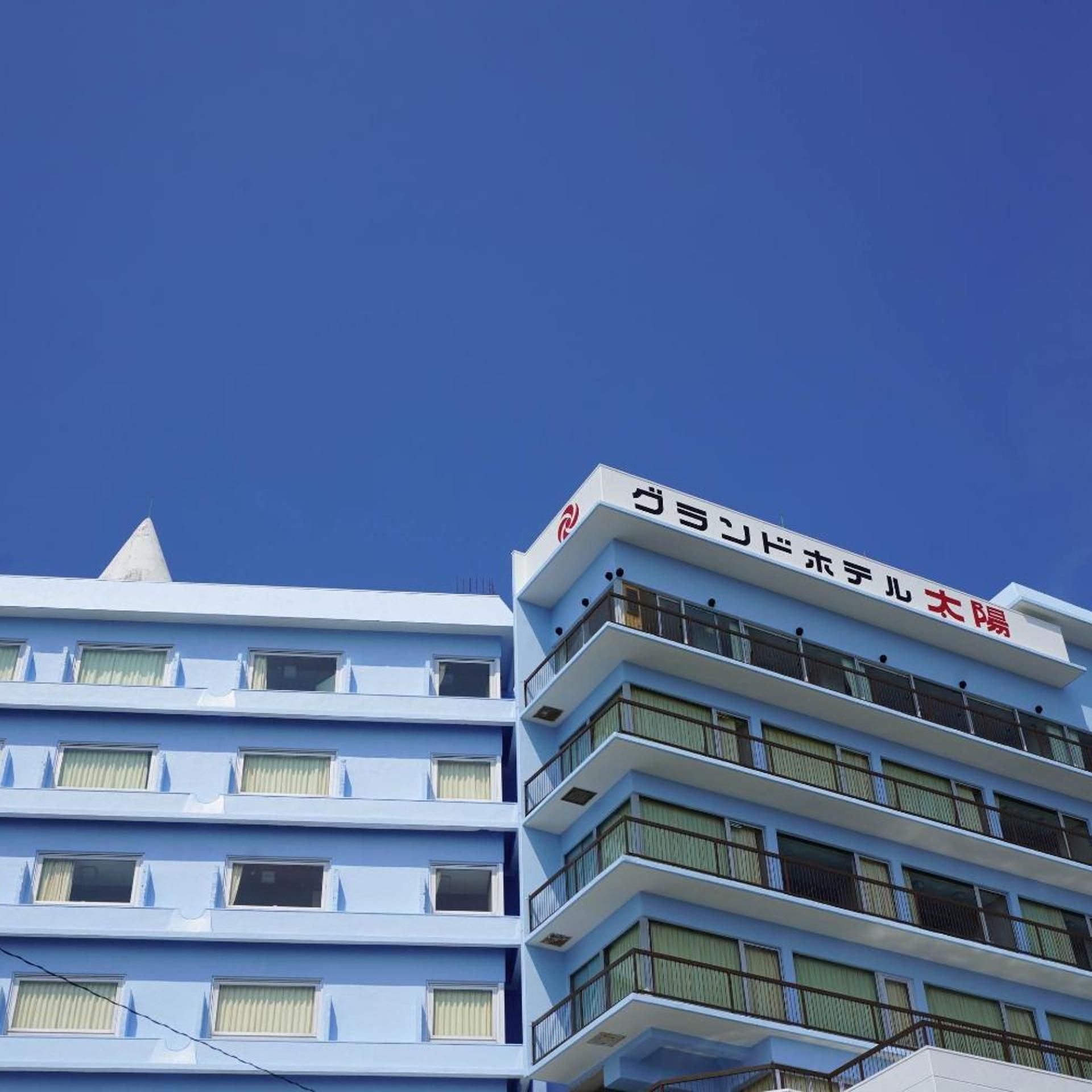 A multi-story building with a flat facade, multiple balconies, and a clear blue sky in the background.