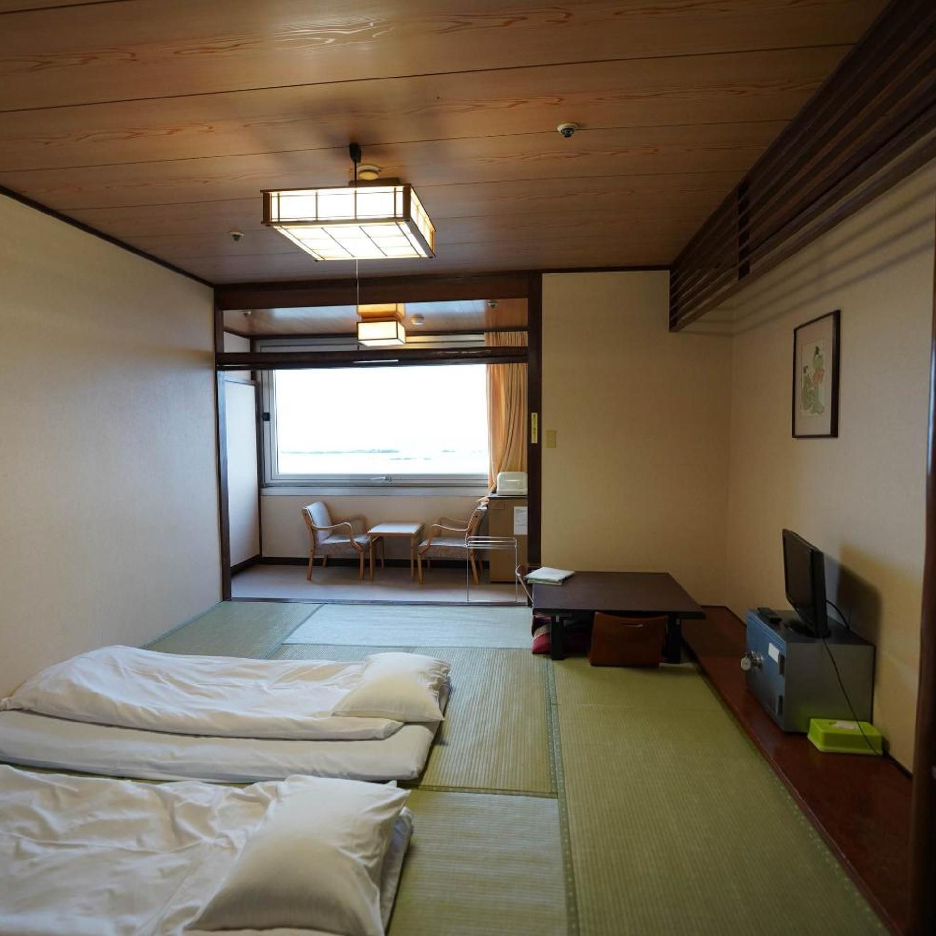 A hotel room with a bed, a desk with a computer, a chair, and a window with curtains.