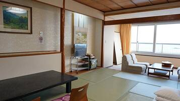 A traditional Japanese-style room with tatami flooring, a low table, cushions, a sofa, and a television.