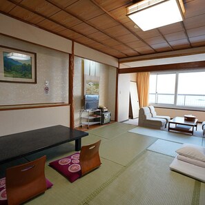 A traditional Japanese-style room with tatami flooring, a low table, cushions, a sofa, and a television. - Grand Hotel Taiyo (Minamiboso)