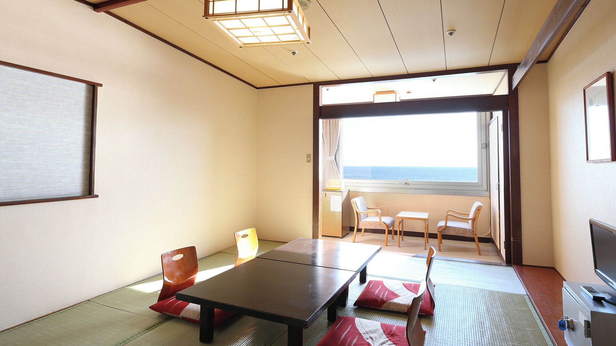 A room with a bed, a table, chairs, a TV, and a view of the sea.