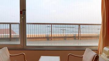 A room with a view of the sea, two chairs, a small table, and a refrigerator.