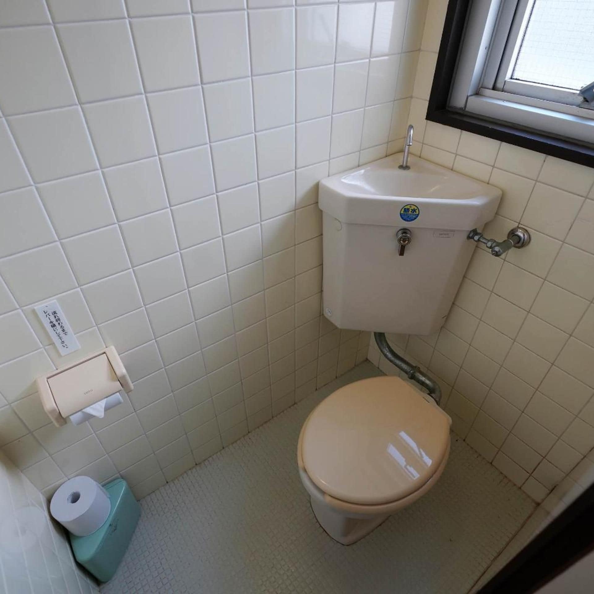 A small bathroom with a toilet, a sink, and a window.