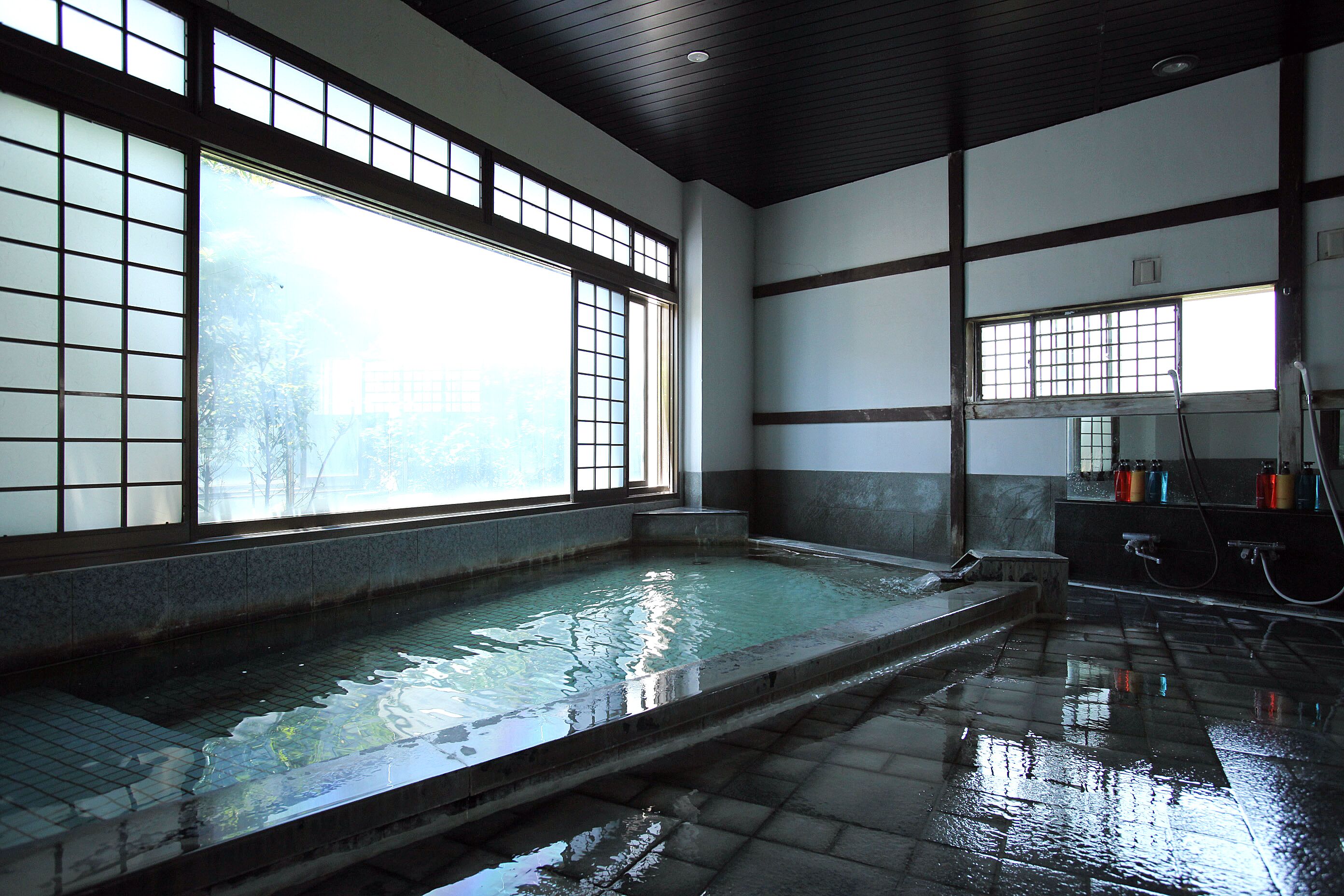 A traditional Japanese onsen with a large wooden window, a stone bath, and a tiled floor.