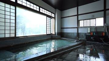 A traditional Japanese onsen with a large wooden window, a stone bath, and a tiled floor.