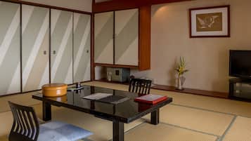 A traditional Japanese-style room with tatami flooring, a low table, chairs, a television, and a framed picture on the wall.