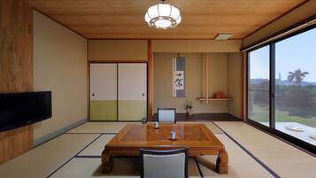 A traditional Japanese-style room with tatami flooring, a wooden table, a television mounted on the wall, and a sliding door.