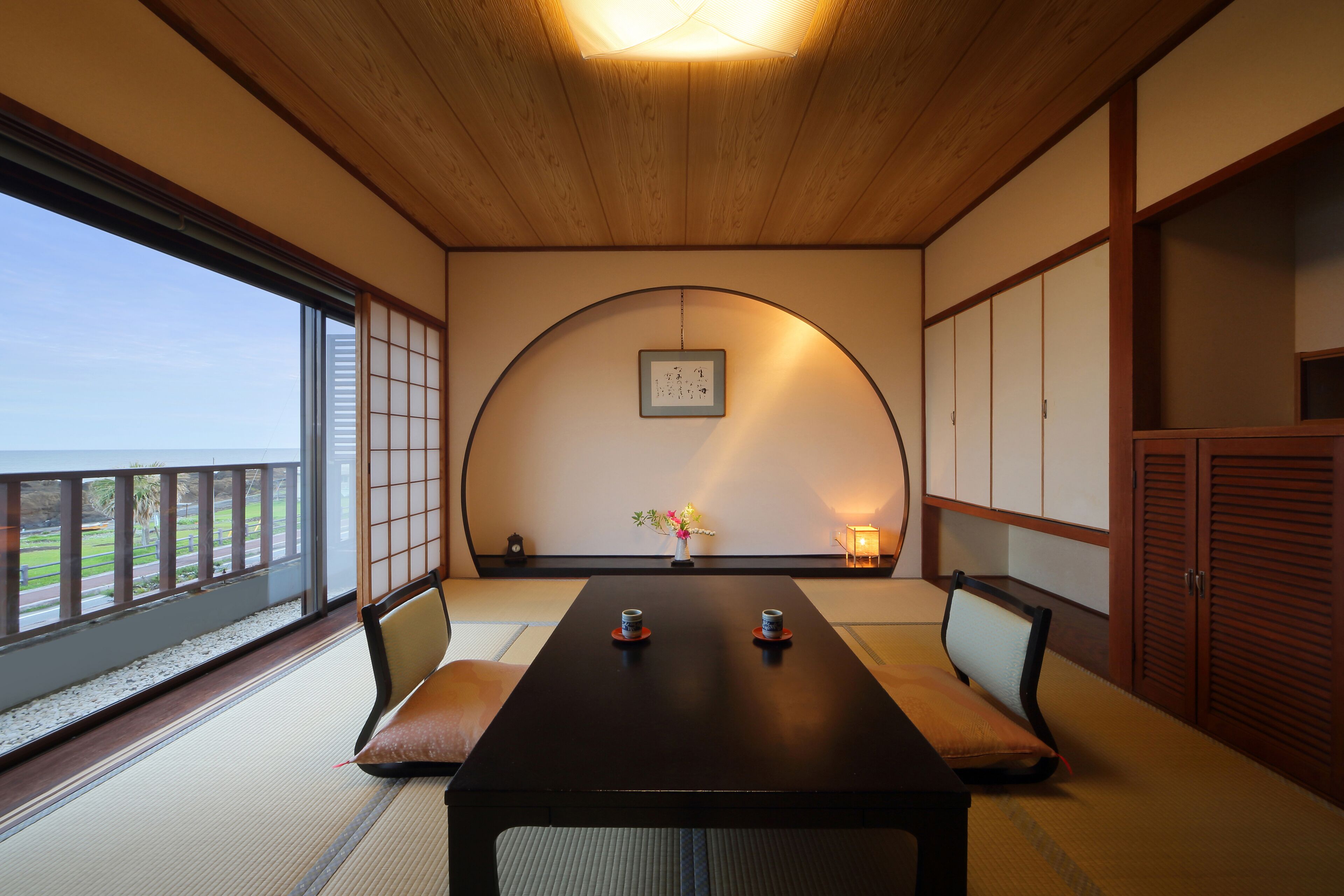 Une pièce de style japonais traditionnel, avec un sol recouvert de tatamis, une table basse avec des coussins, des portes coulissantes et une vue sur un jardin.