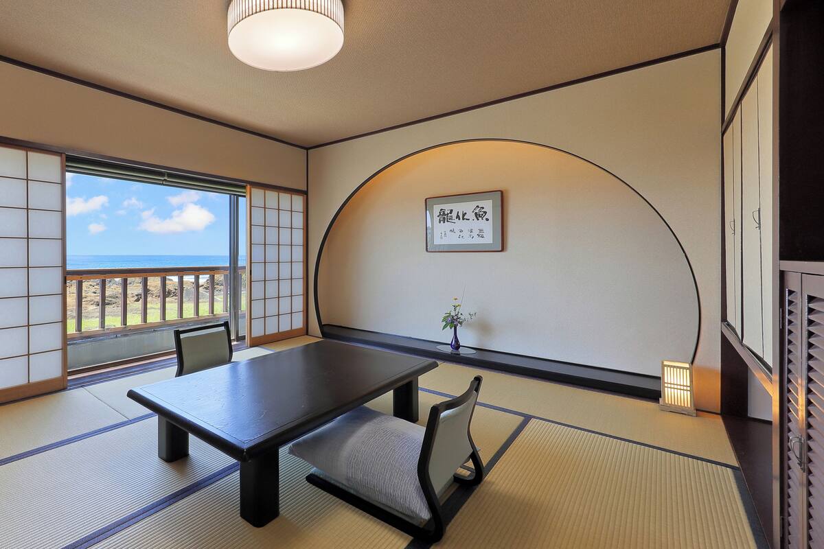 Une pièce de style japonais traditionnel, avec un sol recouvert de tatamis, une table basse et une vue sur l’océan.