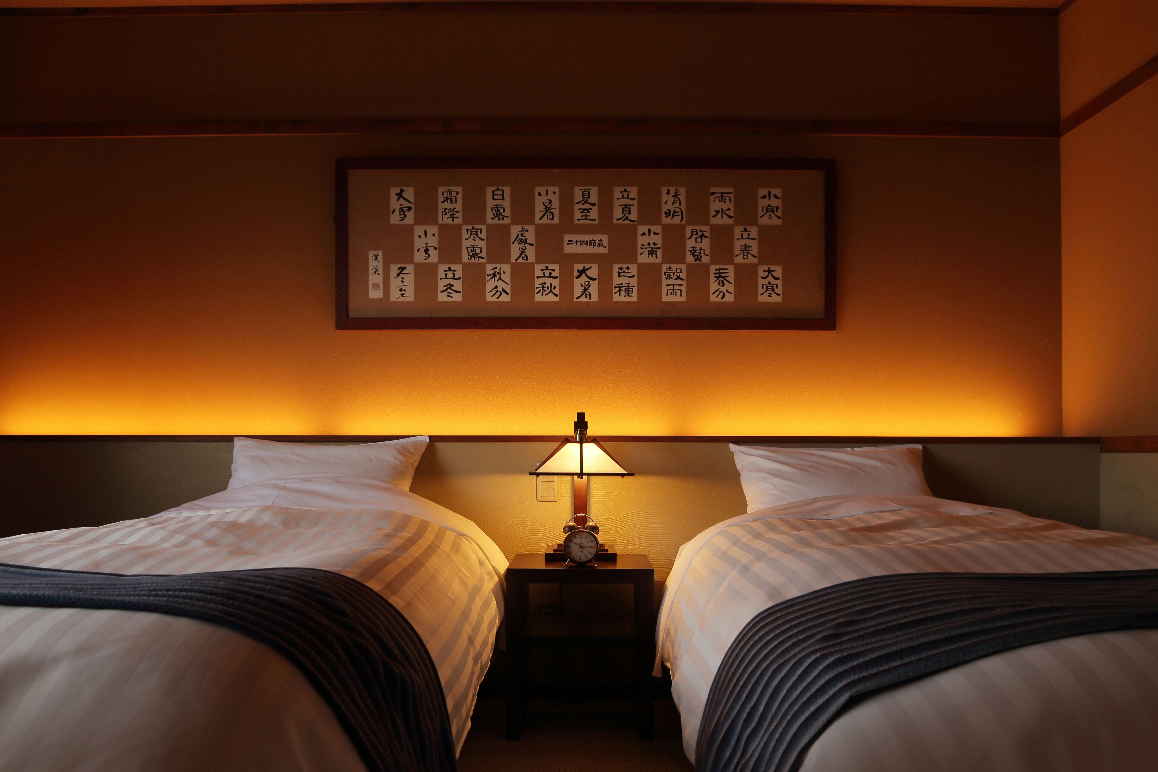 A hotel room with two beds, a nightstand with a lamp, and a wall with Chinese characters.