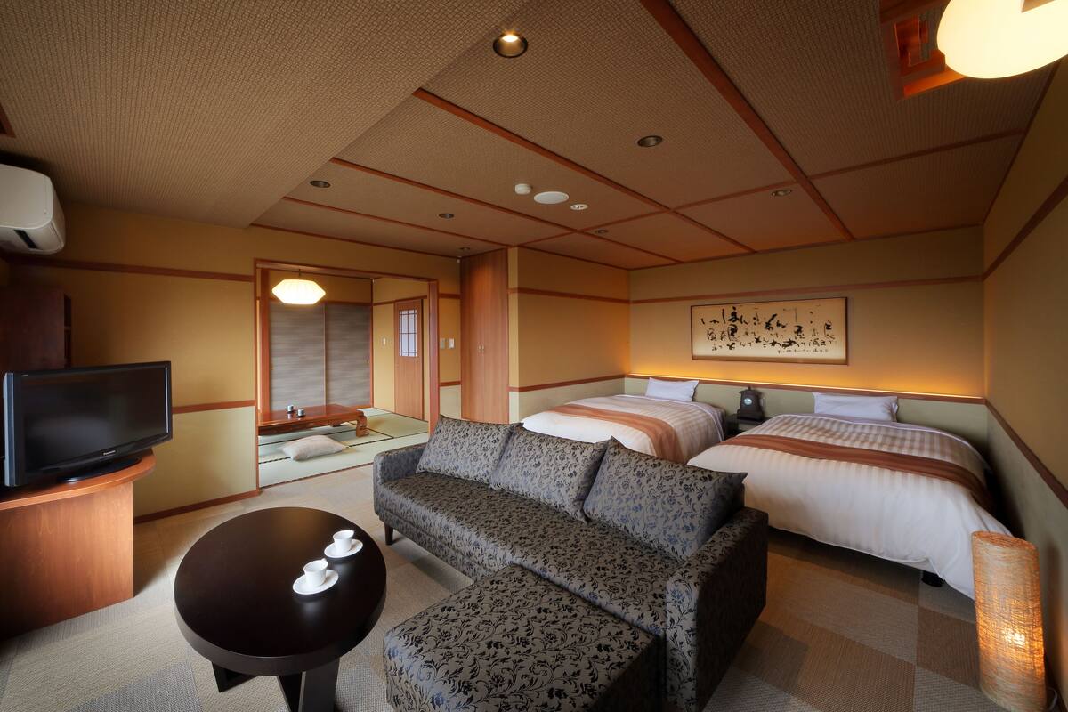 Une chambre d’hôtel avec un canapé, deux lits, une télévision et un tableau au mur.