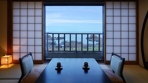 Een traditionele Japanse kamer met tatami vloerbedekking, een lage tafel met twee kopjes, en uitzicht op zee door een shoji scherm.