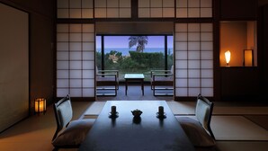 Een traditionele Japanse kamer met tatami vloerbedekking, een lage tafel met kaarsen, en uitzicht op zee door shoji schermen.