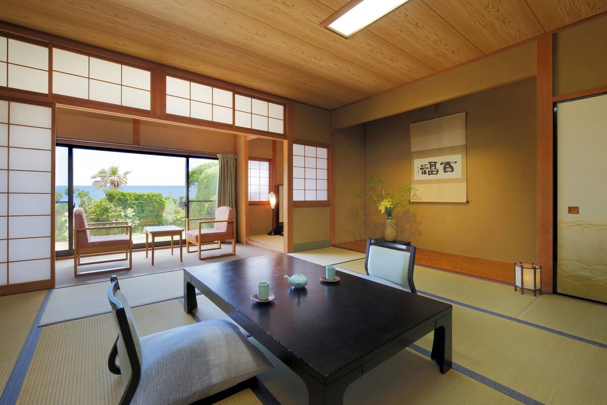 Une pièce de style japonais traditionnel, avec un sol recouvert de tatamis, une table basse et une vue sur l’extérieur.