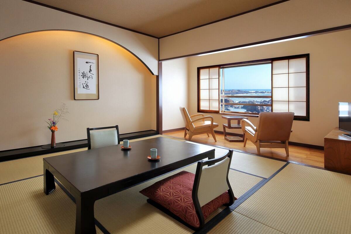 Une pièce de style japonais traditionnel, avec un sol recouvert de tatamis, une table basse et une vue sur la mer à travers un paravent en papier.