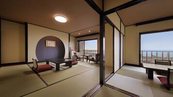 A traditional Japanese room with tatami flooring, a low table, chairs, and a view of the sea through large windows.