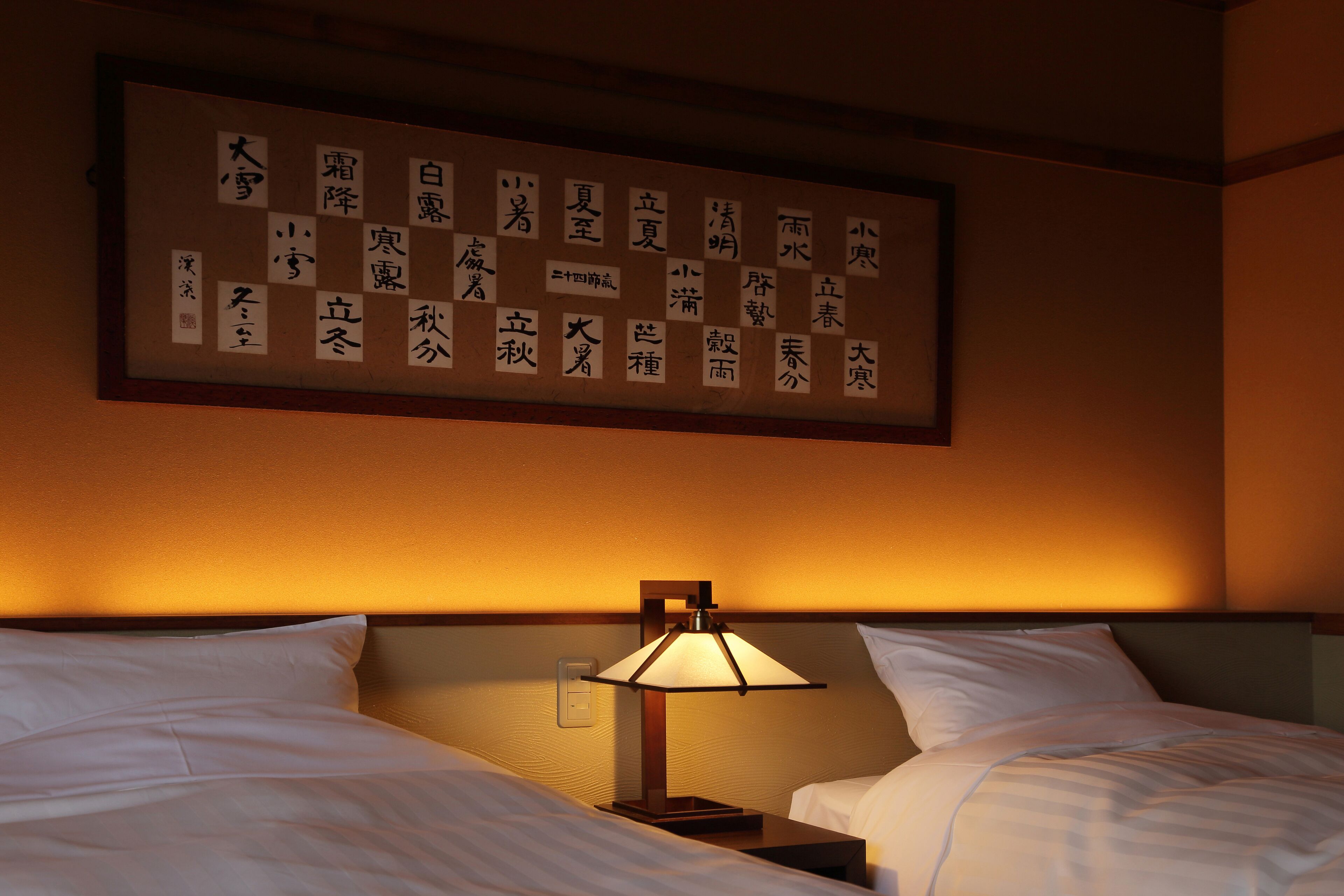 Habitación de hotel con cama, mesita de noche, lámpara y una pared con caligrafía.