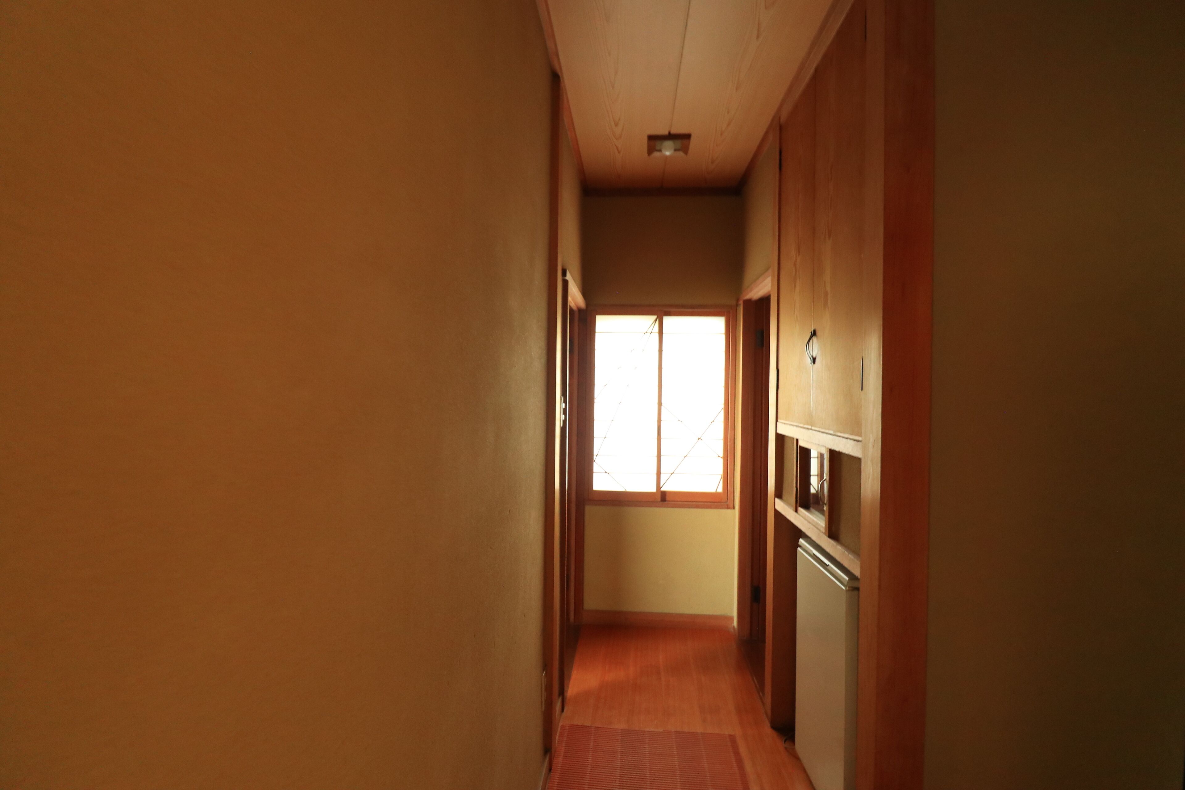 A narrow hallway with wooden walls and a tiled floor, leading to a window with a view of the outside.