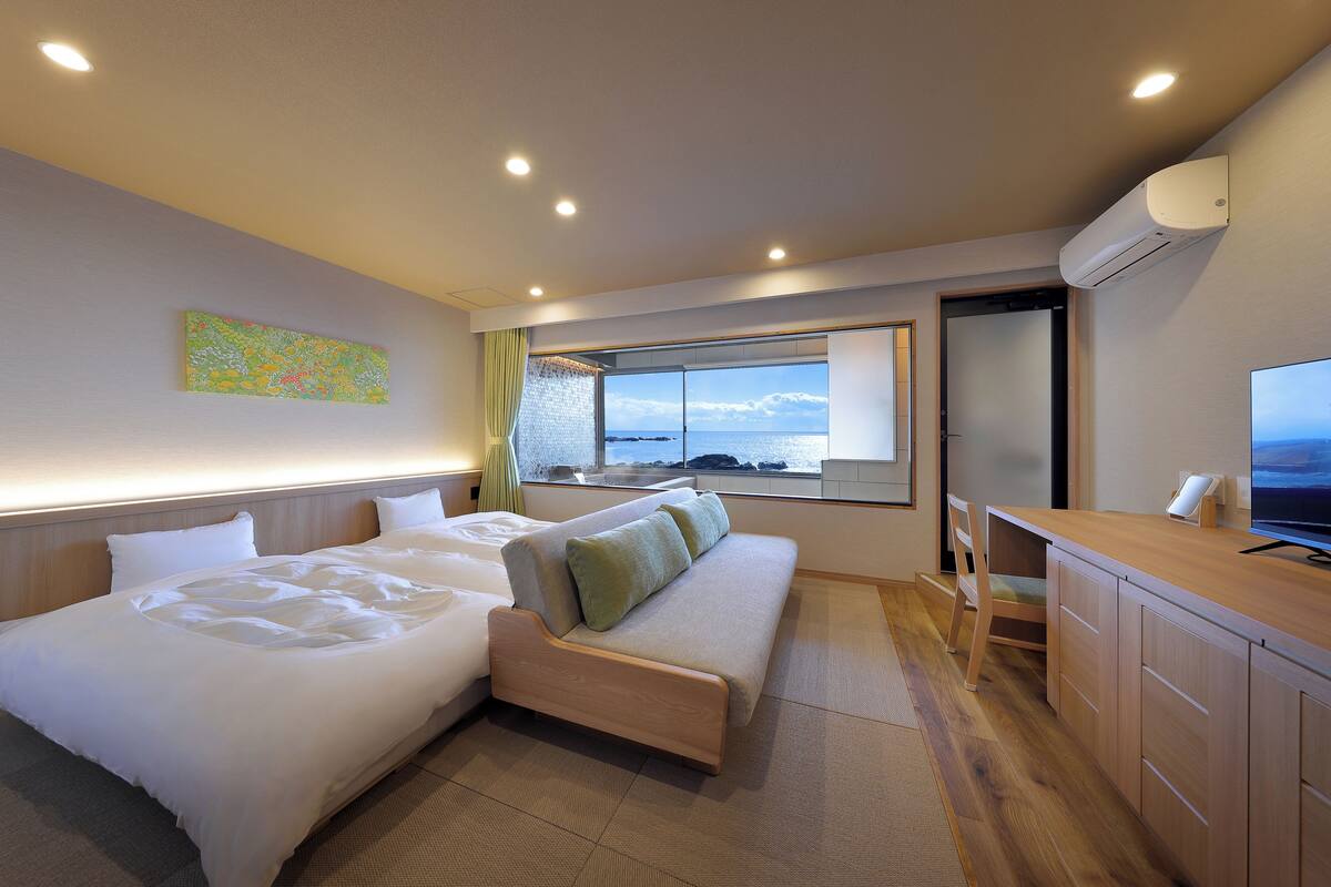 Une chambre d’hôtel avec un lit, un canapé, un bureau et une grande fenêtre donnant sur la mer.