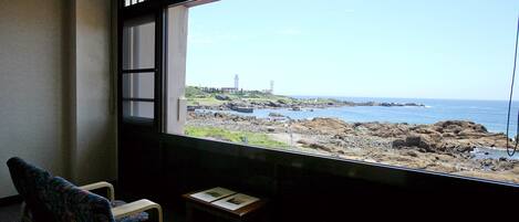 Una habitación con vistas a una costa rocosa, una silla y una pequeña mesa con una placa.