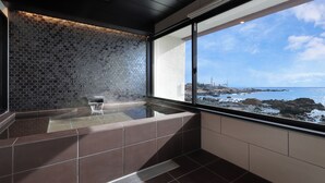 Een moderne badkamer met een glazen badkuip, uitzicht op zee en een betegelde achterwand met een honingraatmotief.