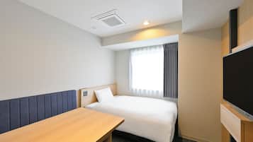 Ein Hotelzimmer mit einem Bett, einem Holztisch, einem Flachbildfernseher und einem Fenster mit Vorhängen.