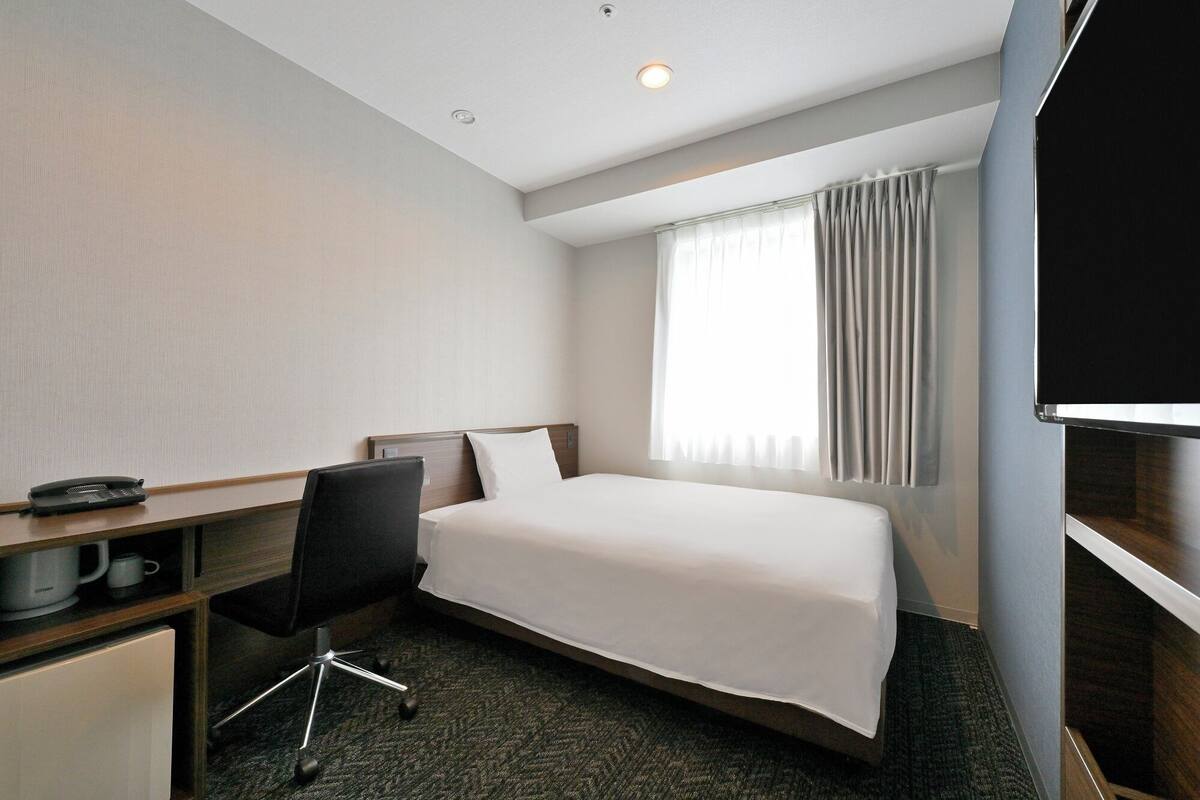A hotel room with a bed, a desk, a chair, a television, and a window with curtains.